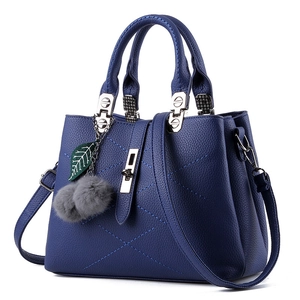 Dark blue leather tote bag with cross stitching, top handle and plush ball charm accessory