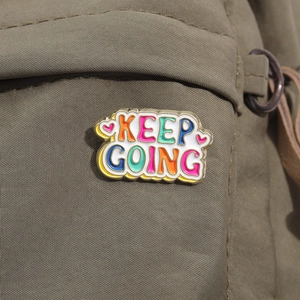 Close-up of Keep Going colorful enamel brooch pin on olive green fabric texture