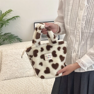 Detail of plush handbag with brown heart patterns and white logo tag held by a model