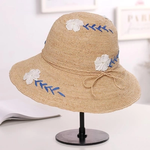 Detail of raffia sun hat with 3D white flower embroidery and blue wavy stitching