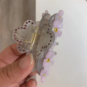 Close-up of translucent gray butterfly hair claw clip with purple rhinestones and pink flowers