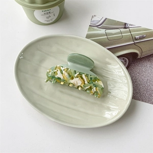 Detail view of a vintage green acetate hair claw clip on an oval ceramic plate