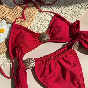Detail of dark red bikini top featuring gold shell hardware accents on holiday background