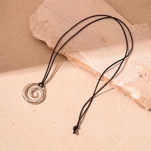 Minimalist spiral donut pendant necklace resting on textured beige stones