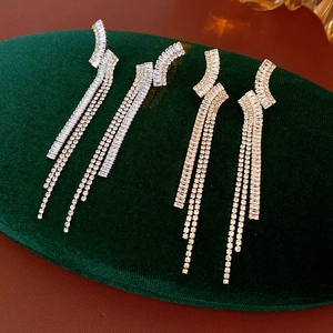 Dettaglio di orecchini a nappa color argento e oro con strass lucidi su velluto verde scuro