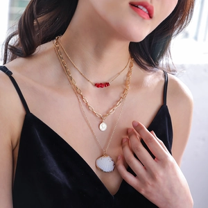 Three-layer gold necklace set with red stones, coin pendant, and shell detail on model