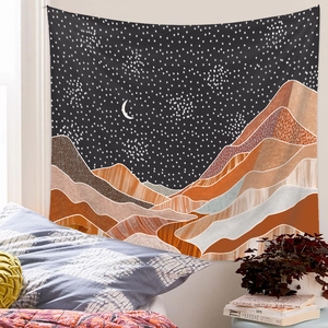 Wall tapestry featuring celestial moon and mountains hanging above a cozy bedroom bed