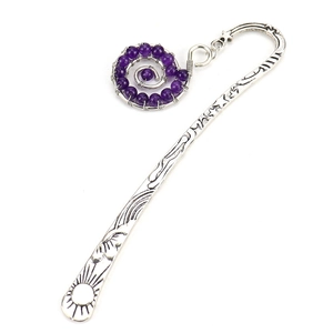 Detailed close-up of antique silver bookmark with celestial engraving and purple crystal pendant