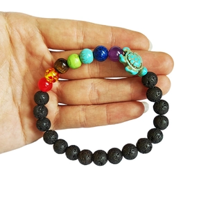 Handheld view of seven chakra lava stone elastic bracelet with a turquoise turtle charm