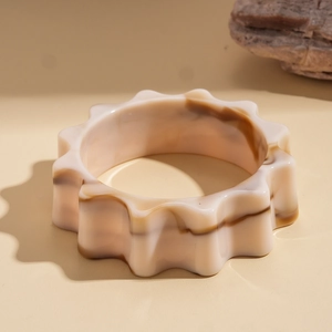 Dettaglio del bracciale largo in acrilico marmorizzato con bordi ondulati su una pietra