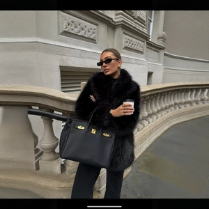 Femme élégante en manteau de fausse fourrure noire avec un grand sac cabas en cuir grainé