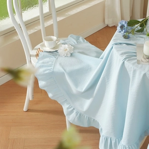 Detailed view of light blue cotton blend tablecloth with elegant ruffled edge and soft drape