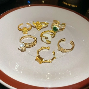 Detailed close-up of gold-plated multi-layer rings with zircon, emerald, and pearls in a dish