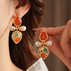 Close-up of vintage gold earrings with orange gemstones and white pearls on ear