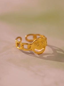 Dettaglio anello a catena dorata con charm smiley occhi a cuore su fondo rosa