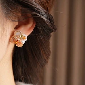 Detail of vintage flower pearl earrings with orange zircon and gold chain trim on ear