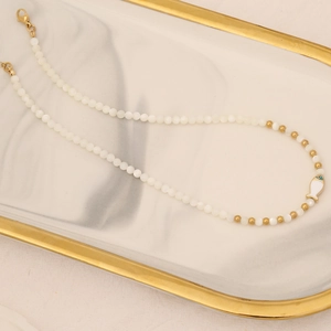 Elegant gold fish pendant necklace with white pearls and gold beads on marble tray