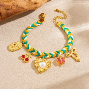 Handmade woven cord bracelet with gold plated cherry and heart charms on a sandy surface