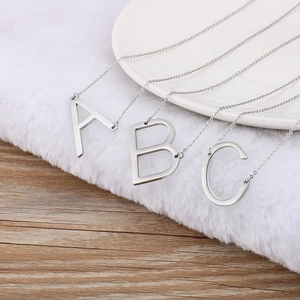 Sleek silver stainless steel initial necklaces A, B, C on a luxury white plush background