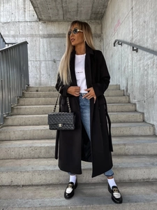 Chic long black wool coat styled with blue skinny jeans and stylish loafers outdoors