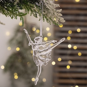 Clear acrylic ballerina ornament hanging on a snowy branch with festive bokeh lights