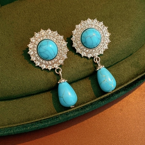 Detail view of silver drop earrings with turquoise stones and rhinestones on leather background