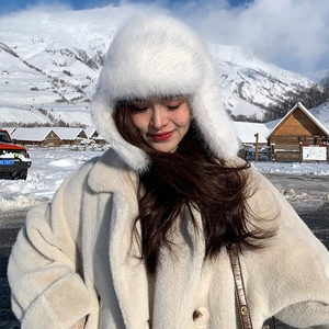 Detail view of white faux fur trapper hat and beige plush coat against a snowy mountain