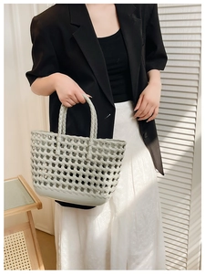 Detail of light green hollow woven basket bag held by a model in natural light