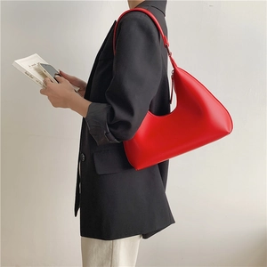 Side view of a red minimalist crescent moon shoulder bag on a model in a black suit