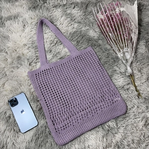 Detail of purple knitted tote bag with hollow mesh pattern on a gray faux fur rug