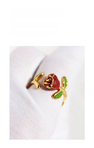 Detailed view of handmade red enamel rose ring worn on a gloved hand with gold band