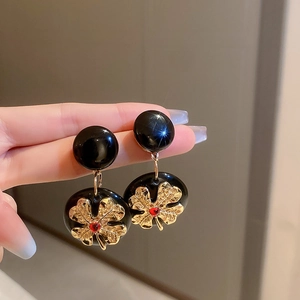 Macro shot of black geometric earrings featuring golden leaf detail and red rhinestone
