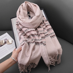 Pink cashmere-like scarf with gray and brown stripes and fringe on a gray sofa