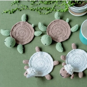 Handmade crochet turtle and sheep coasters with intricate knit textures on a desk