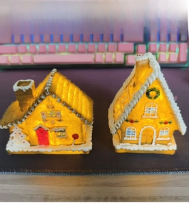 Detail of two LED Christmas resin gingerbread houses with glowing warm lights and snow decor