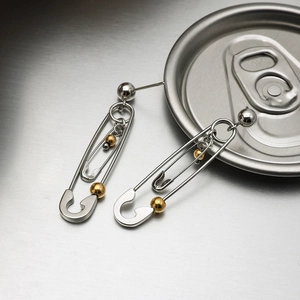 Detailed close-up of silver paperclip earrings with gold beads on a brushed metal surface