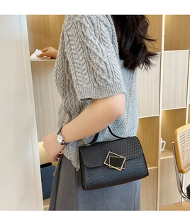 Detalle de la textura en relieve y hebilla dorada en un bolso bandolera negro de moda