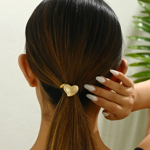 Detail of a vintage golden heart charm on a black hair tie worn in a ponytail