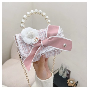 Close-up of pink tweed girl's handbag with pearl handle, ribbon bow and camellia detail