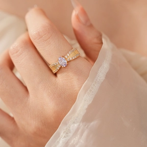 Nahaufnahme eines goldenen Rings mit lila Edelstein und Zirkonia auf einer Modelhand
