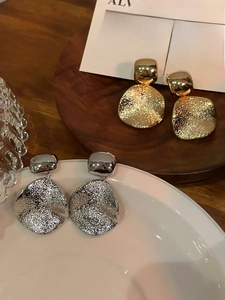 Détails de boucles d'oreilles carrées en métal martelé doré et argenté sur plateau