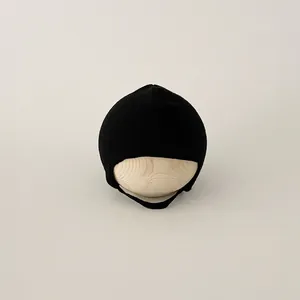 Detail of black knitted baby hat with earflaps and chin straps on wooden display