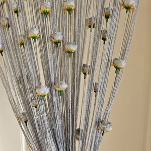 Close-up of silver string curtain with decorative white and yellow flower ornaments