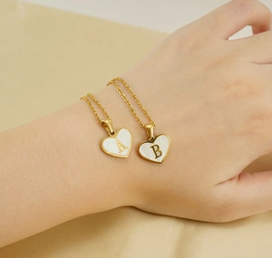 Detail of heart shell necklaces with initials A and B on soft beige fabric background