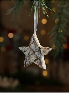 Detail of star-shaped birch bark ornament hanging on a pine branch with warm bokeh lights