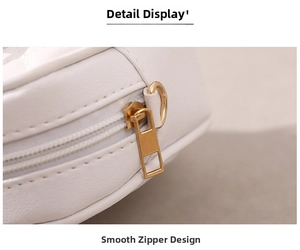 Detailed close-up of the smooth gold metal zipper and D-ring on a white leather bag