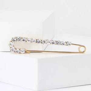 Elegant gold safety pin brooch with sparkling clear rhinestones on white geometric stands