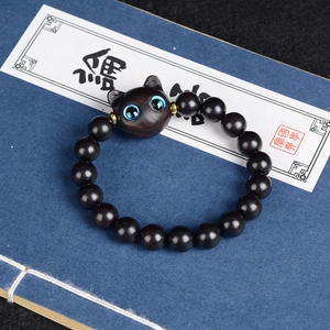 Bracelet en bois sombre avec breloque chat aux yeux bleus sur fond de livre ancien