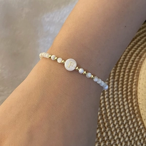 Close-up of beaded letter F bracelet featuring white pearls and gold accents on wrist