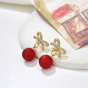 Elegant gold bow earrings with small diamonds and matte red hanging pearls on a tray